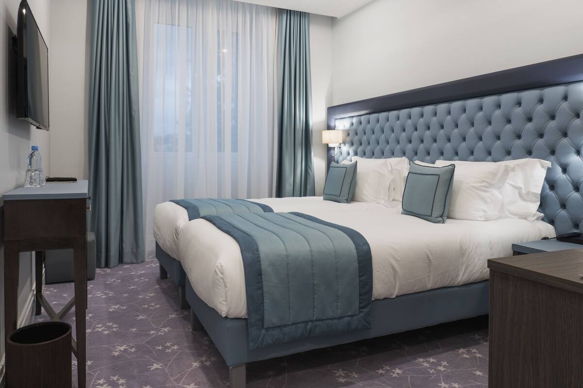 Une chambre d’hôtel avec un grand lit, une table de chevet, une télévision et une fenêtre avec des rideaux.