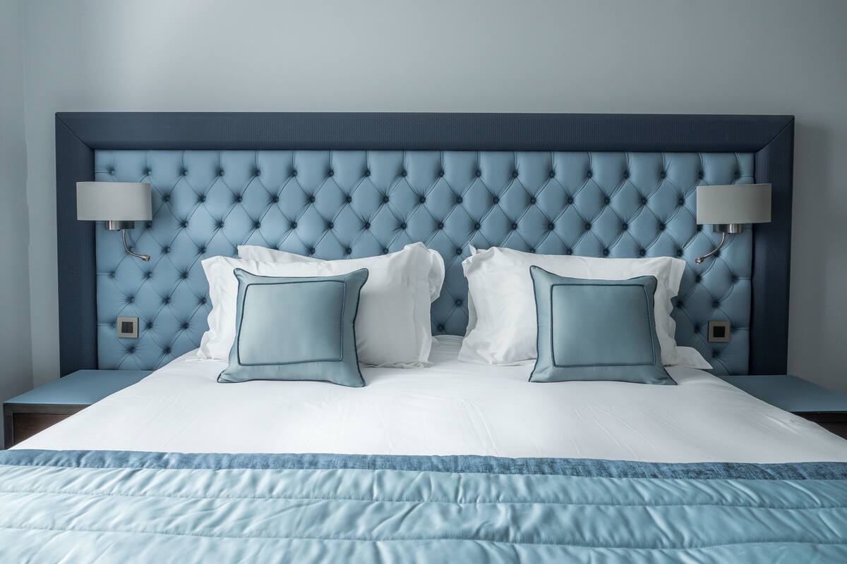 Un lit avec une tête de lit capitonnée, deux lampes de chevet et une couvre-lit bleue.