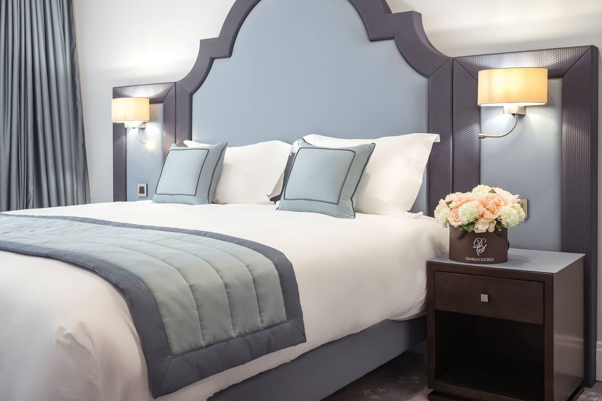 Une chambre d’hôtel avec un grand lit, deux lampes de chevet, une table de chevet ornée d’un vase de fleurs et une tête de lit sombre.