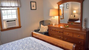 Une chambre à coucher avec un lit, une commode, une chaise, une fenêtre avec des rideaux et un miroir.
