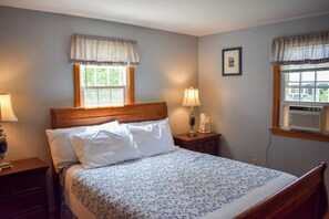 A bedroom with a wooden bed, two bedside tables with lamps, a window with a valance, and a framed picture on the wall. - Ranch home with screened sunporch just 7/10 miles to Dennisport beaches. (Dennis Port)