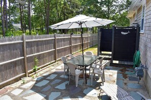 A patio with a glass table and chairs, an umbrella, and a wooden fence. - Ranch home with screened sunporch just 7/10 miles to Dennisport beaches. (Dennis Port)