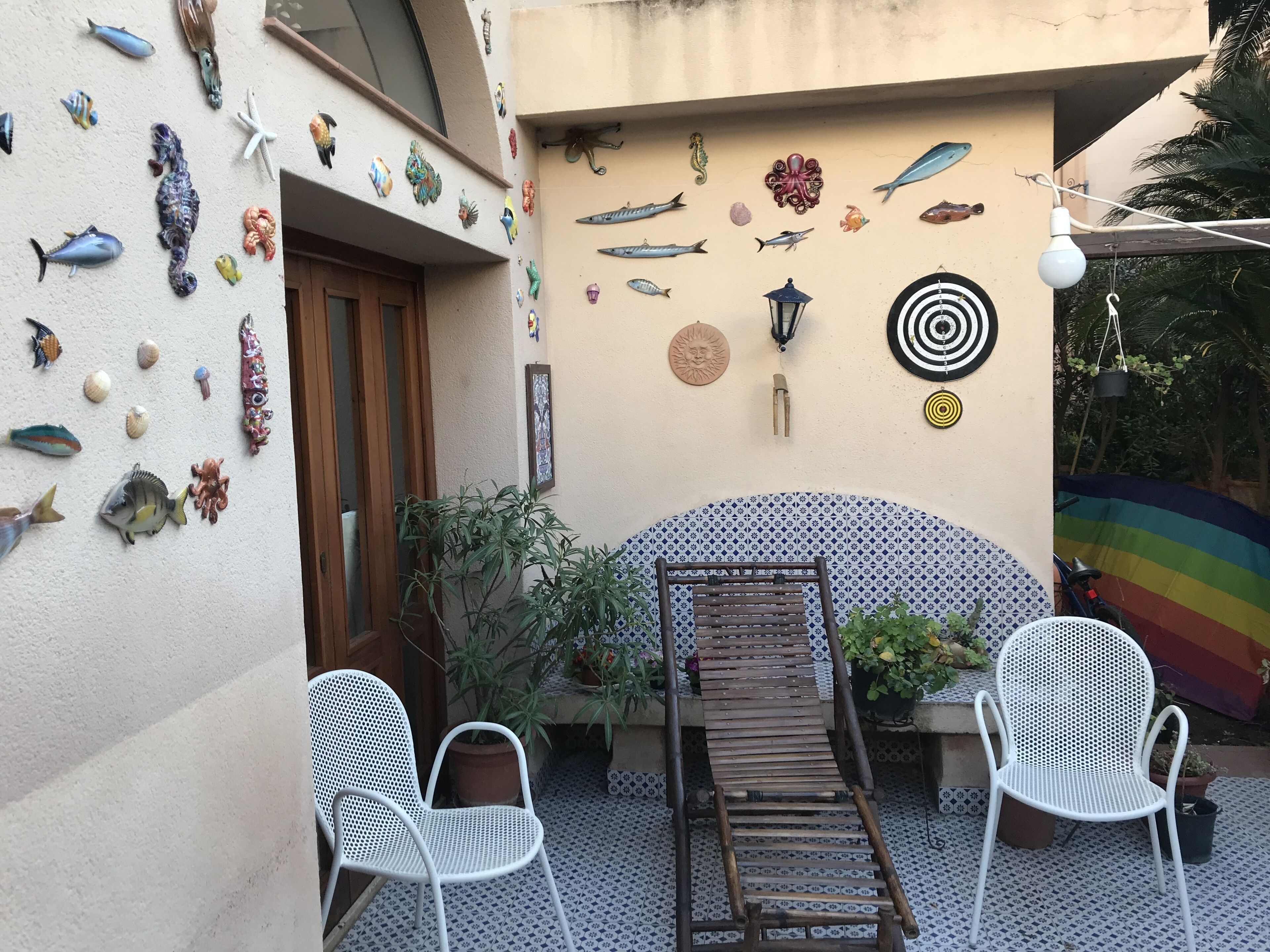 Une terrasse avec deux chaises blanches, un banc en bois et un mur décoré de divers ornements représentant des poissons et des créatures marines.