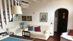 A living room with a white sofa, a dining table with chairs, a lamp, and a painting on the wall. - Holiday home the fish house (Palermo)