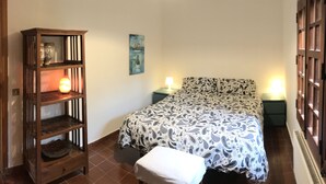 A bedroom with a bed, a nightstand, a bedside table, a wooden shelf, and a wall-mounted lamp. - Holiday home the fish house (Palermo)