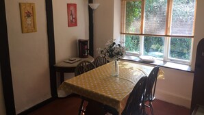 Uma área de refeições com uma mesa posta para dois, uma máquina de café e um vaso com flores.