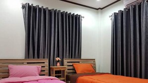 Une chambre avec deux lits, des rideaux foncés, une petite table avec un vase et une tête de lit en bois.