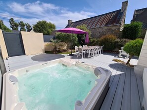 A hot tub with a wooden deck, a dining table with chairs, and a purple umbrella. - Villa Ty Mam'Goz, Brittany Santec spa, indoor swimming pool, 50 m from the beach. (Santec)