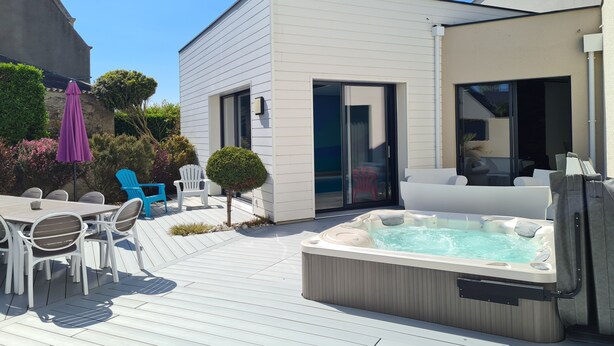 Une terrasse extérieure moderne, dotée d’un jacuzzi, de meubles blancs et surplombant un ciel bleu azur.