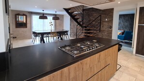 Une cuisine moderne dotée d’un îlot central, d’un coin repas avec une table et des chaises, et d’un escalier menant à un niveau supérieur.