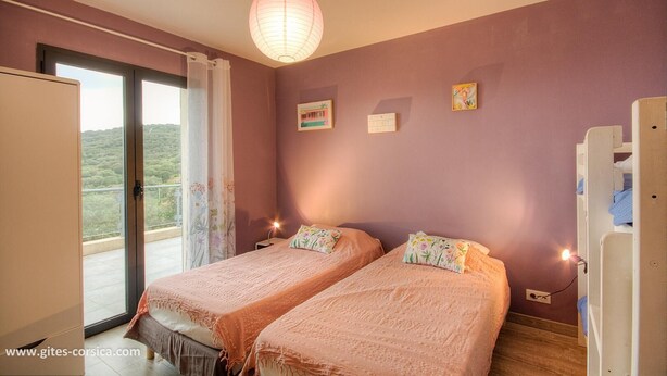 Een slaapkamer met twee bedden, een glazen schuifdeur naar het balkon, een hanglamp en een klein nachtkastje met een lamp.