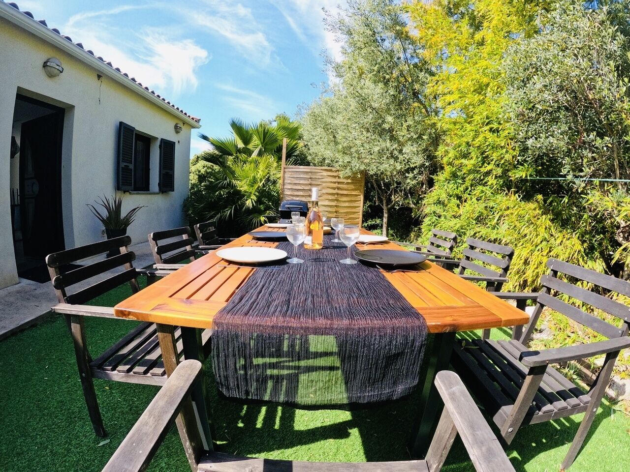 Un'area pranzo all'aperto con tavolo e panche in legno, immersa nel verde con un edificio sullo sfondo.