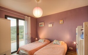 Une chambre avec deux lits, une porte-fenêtre coulissante donnant sur le balcon, un luminaire suspendu et une petite table de chevet avec une lampe.