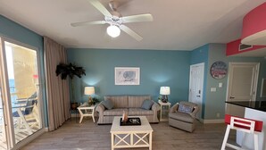 A living room with a ceiling fan, a striped sofa, a coffee table, and a dining area with a red chair. - Gulf-Front Calypso 1BR/2BA | Free Beach Service (Panama City Beach)
