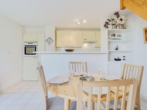Een compacte keuken met witte kasten, een inbouwoven en een eethoek met een ronde houten tafel en vier stoelen.