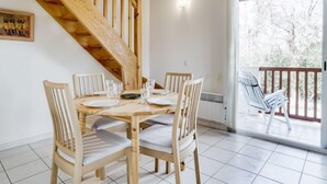 A dining area with a wooden table and chairs, a staircase, and a view through a glass door to an outdoor balcony. - Les écureuils by Interhome (Capbreton)