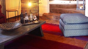 A cozy living room with a wooden bench, a patterned ottoman, a birdcage with candles, and a large chandelier. - Agriturismo La Striscia (Arezzo)