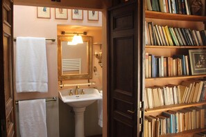 A bathroom with a white sink, a mirror, and a towel rack. There is a bookshelf with books to the right. - Agriturismo La Striscia (Arezzo)