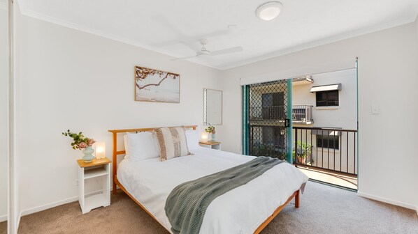 Une chambre à coucher comprenant un lit, des tables de chevet, un ventilateur de plafond, une fenêtre et un balcon avec une balustrade.
