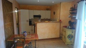 A compact kitchen with white cabinets, a tiled floor, and a dining table with chairs. - Gîte "La Terrasse". A real "Eagle's Nest" for two people. (Beaumont)