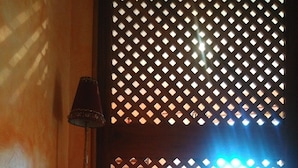 A room with a bed, a nightstand, and a window with a lattice screen. - Gîte "La Terrasse". A real "Eagle's Nest" for two people. (Beaumont)