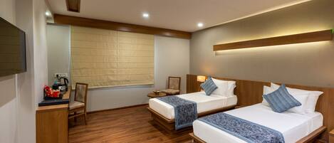 Habitación de hotel con dos camas, suelo de madera, un escritorio con silla, televisión y ventana con persianas.