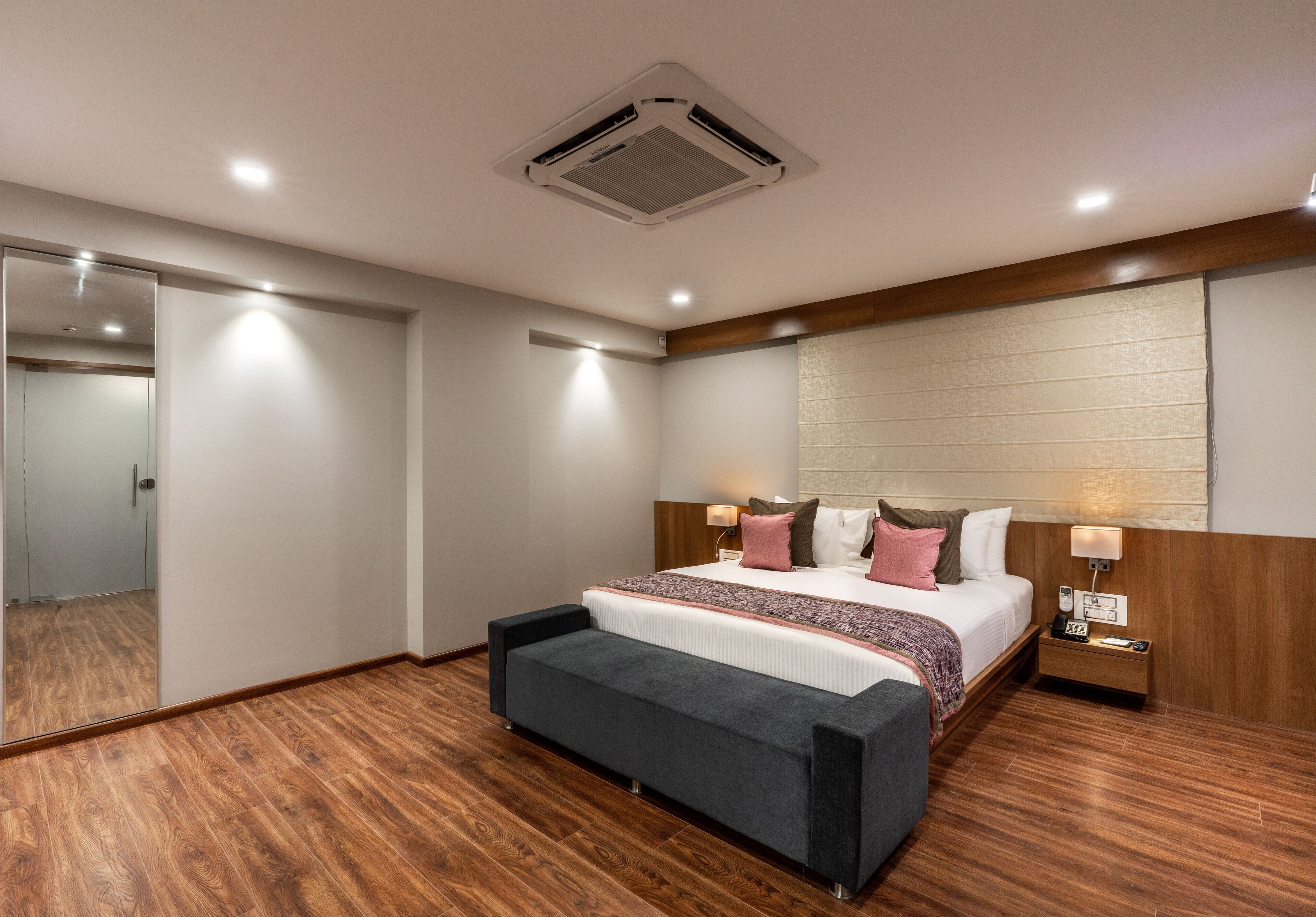 A modern hotel room with a large bed, bedside tables, a mirror, and a wooden floor.