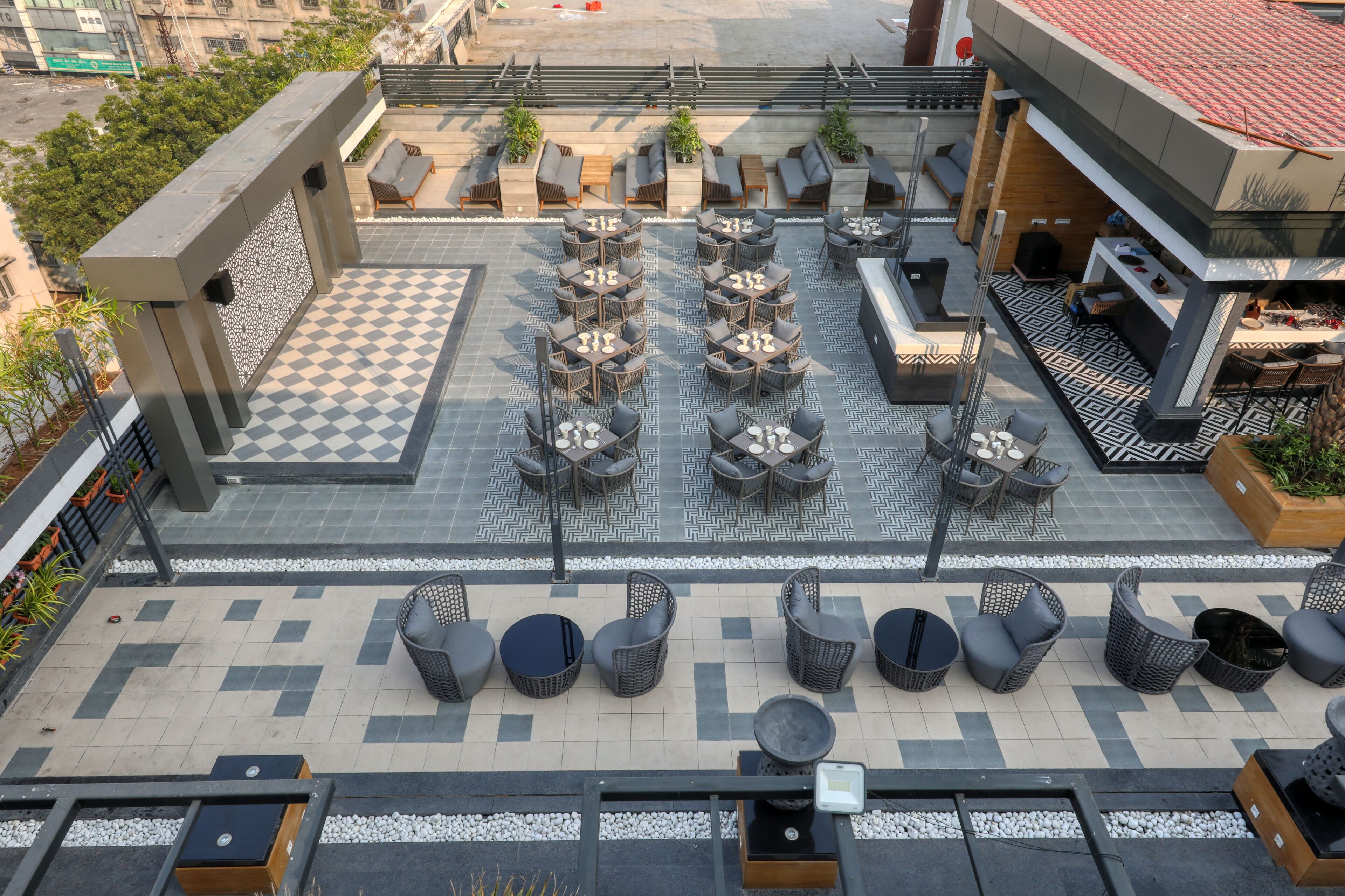 Terraza en la azotea con varias zonas de estar, que incluyen mesas redondas y sillones, sobre un suelo con diseño de cuadros.