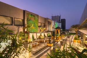 An outdoor patio area with seating arrangements, planters, and a wall with greenery. - Hotel Delice (Bhilwara)