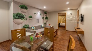 Una sala de estar moderna con una mesa de comedor de cristal, sillas de madera, un sofá gris y plantas colgantes.