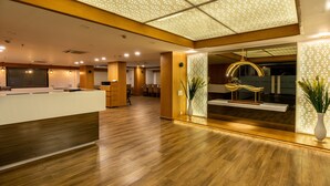 Un moderno vestíbulo de hotel con un mostrador de recepción de madera, una zona de estar y una pared decorativa con patrones geométricos.