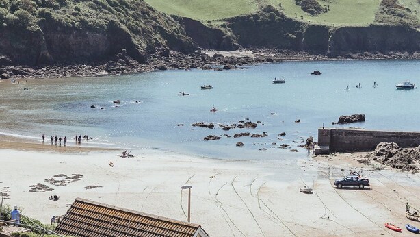 A coastal beach with boats, a sandy shore, and a hill in the background.