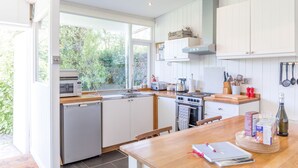 A modern kitchen with white cabinets, a wooden countertop, and a view of greenery outside.