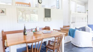 A dining area with a wooden table and chairs, a bottle of wine, and a laptop.