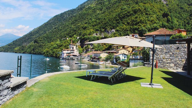 A lakeside property with a grassy lawn, a pool with lounge chairs, and a mountain backdrop. - Luxury San Rocco near BELLAGIO (Lezzeno)