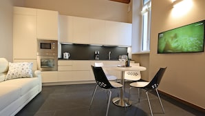 A modern kitchen with white cabinets, a built-in microwave, and a coffee maker. There is a dining table with four chairs and a TV mounted on the wall. - Luxury San Rocco near BELLAGIO (Lezzeno)