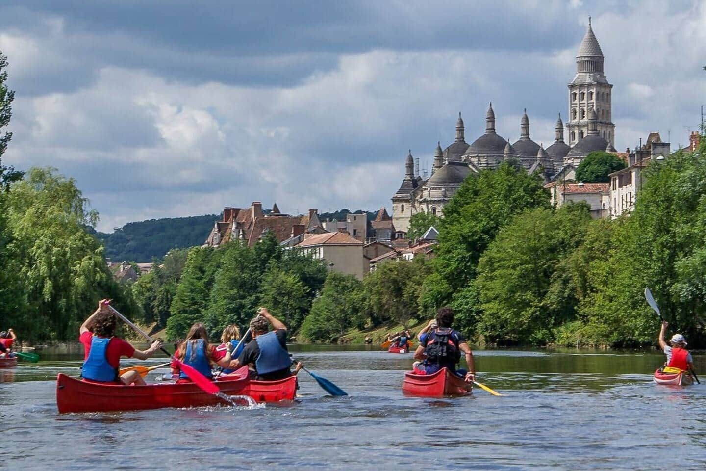 A group of people kayaking on a river with a historic building in the background.