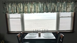 A dining area with a table set for four, two chairs on each side, a window with blinds, and a view of the sea. - Beautiful house right at the beach (Oak Harbor)