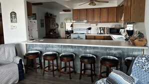 A kitchen with wooden cabinets, a bar area with stools, and a ceiling fan. - Beautiful house right at the beach (Oak Harbor)