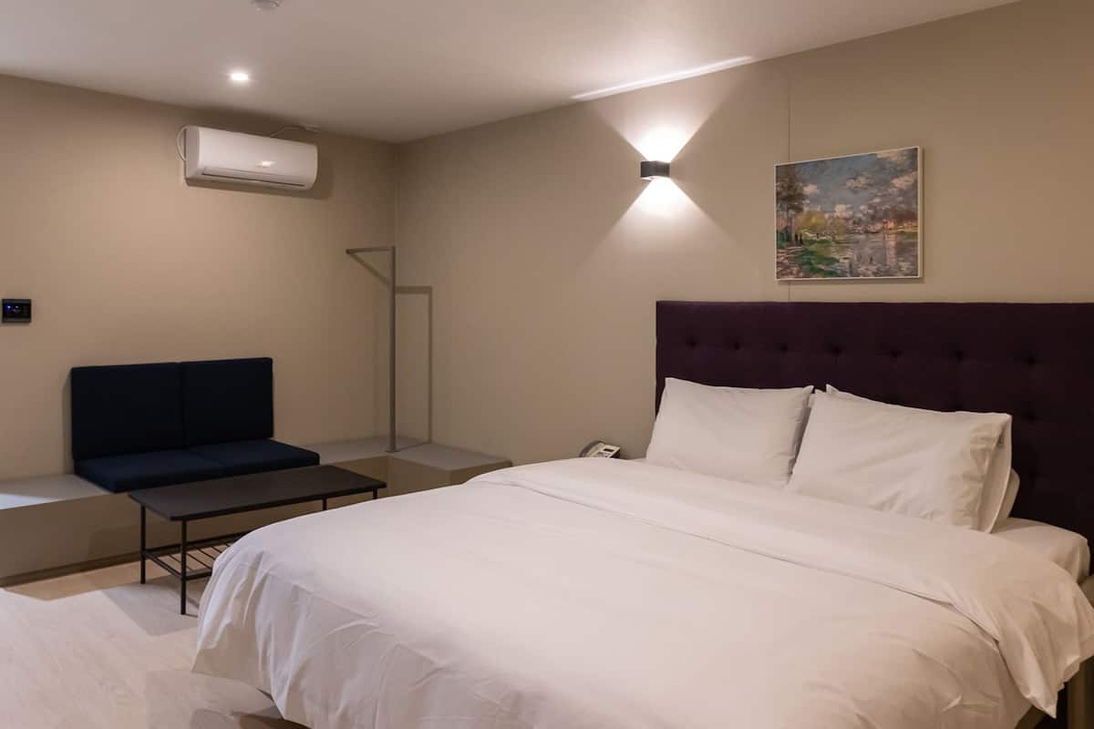 Ein Hotelzimmer mit Bett, Sitzgelegenheit, Klimaanlage, einem Gemälde an der Wand und einer Leuchte.