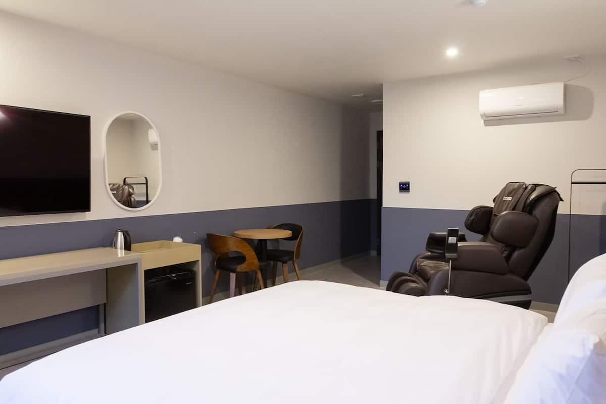 Ein Hotelzimmer mit Bett, Schreibtisch, Sessel, Massagesessel, Fernseher und Klimaanlage.