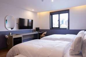 Une chambre d’hôtel avec un lit, un bureau équipé d’un ordinateur, une télévision et une fenêtre donnant sur la ville.