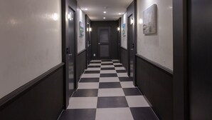 Ein Hotelkorridor mit Schachbrettfußboden, dunklen Wänden und Türen mit Lichtschaltern.