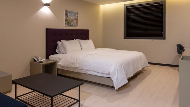 Ein modernes Hotelzimmer mit Bett, Nachttisch und kleinem Schreibtisch.