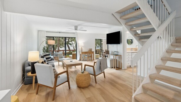 A spacious living area with a sofa, chairs, a dining table, and a staircase. - 2135 Beachwood - Delightful Town-home with calming views in a Relaxed Setting (Fernandina Beach)