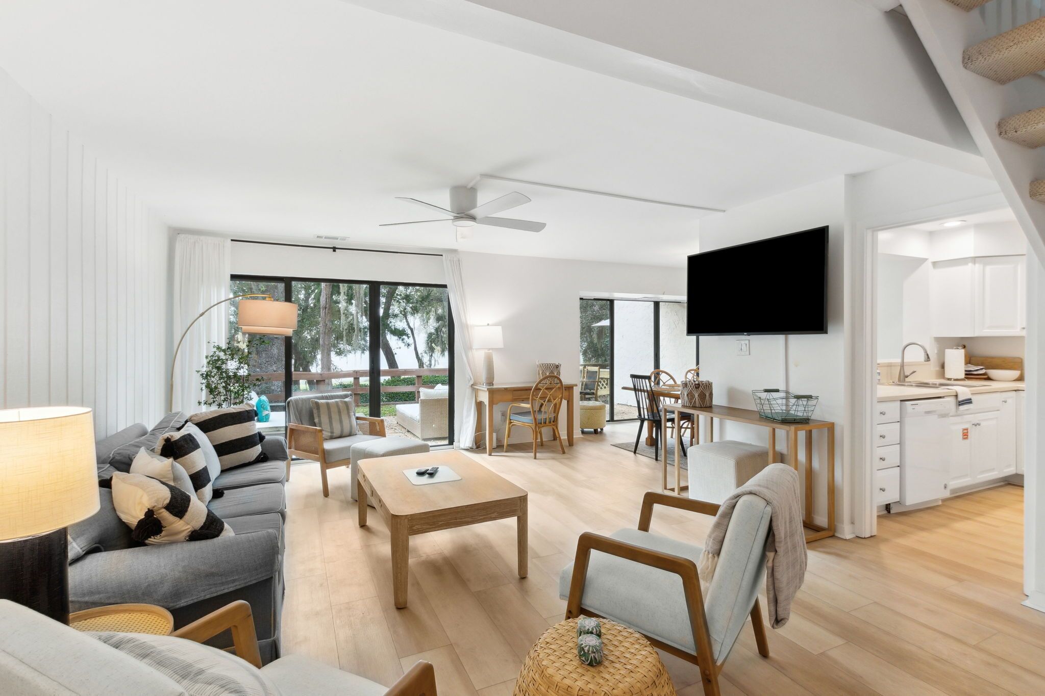 Ein modernes Wohnzimmer mit Sofa, Couchtisch und Sesseln, ein Essbereich mit Tisch und Stühlen, eine Küche mit Schränken und einem an der Wand befestigten Fernseher.