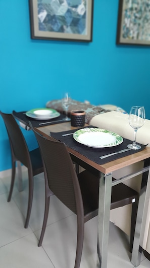 A dining area with a table set for two, featuring a framed painting and a candle holder.