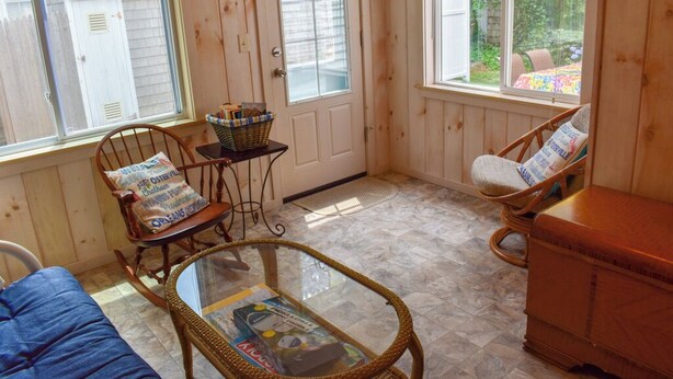 A cozy room with a rocking chair, a glass table, and a wicker chair. A wooden cabinet is visible in the corner. - 2 bedroom cottage just a short walk to Swan River (Dennis Port)