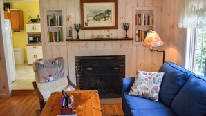 A cozy living room with a fireplace, a blue sofa, and a bookshelf filled with books. - 2 bedroom cottage just a short walk to Swan River (Dennis Port)
