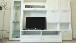 A white entertainment center with a flat-screen TV, glass-fronted cabinets, and drawers.